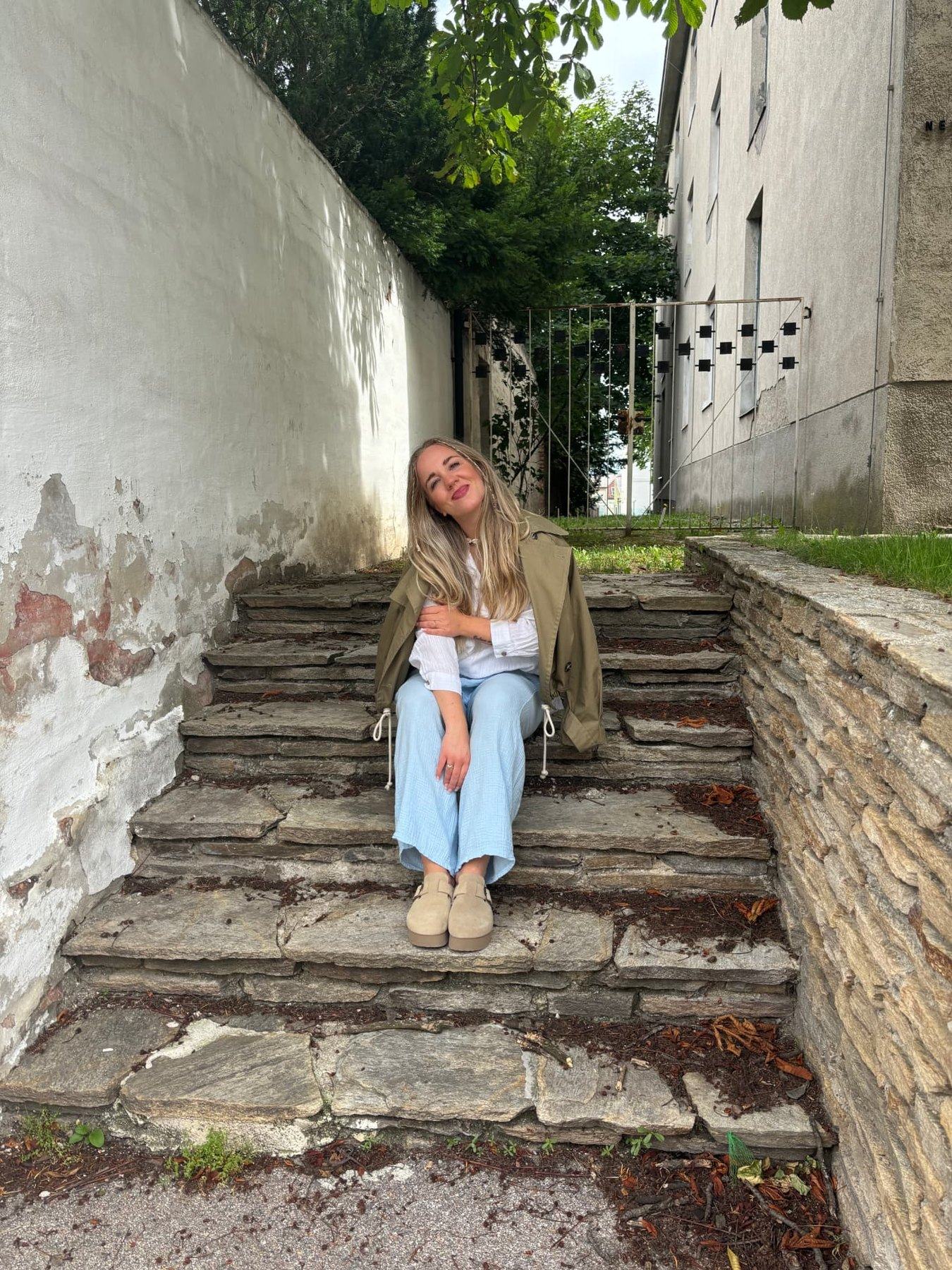 Sabrina sitzt entspannt auf einer alten Steintreppe in einer begrünten Gasse