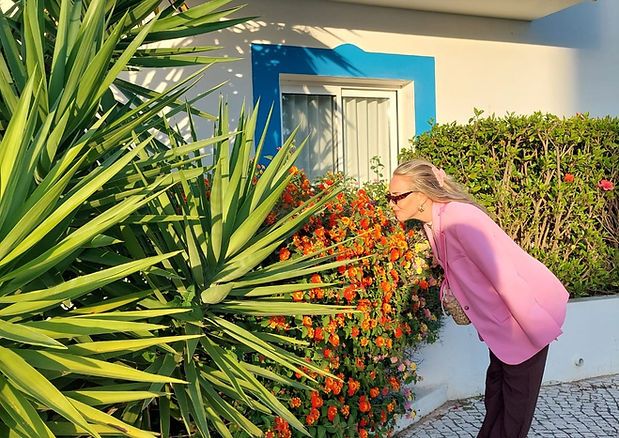 Sabrina Mönch riecht an orangefarbenen Blüten vor einem blauen Haus in Portugal