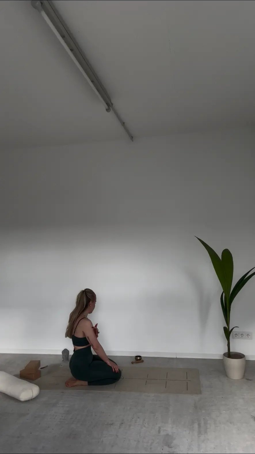 Sabrina sitzt meditierend auf der Korkmatte im hellen Studioraum mit Klangschale und Pflanze