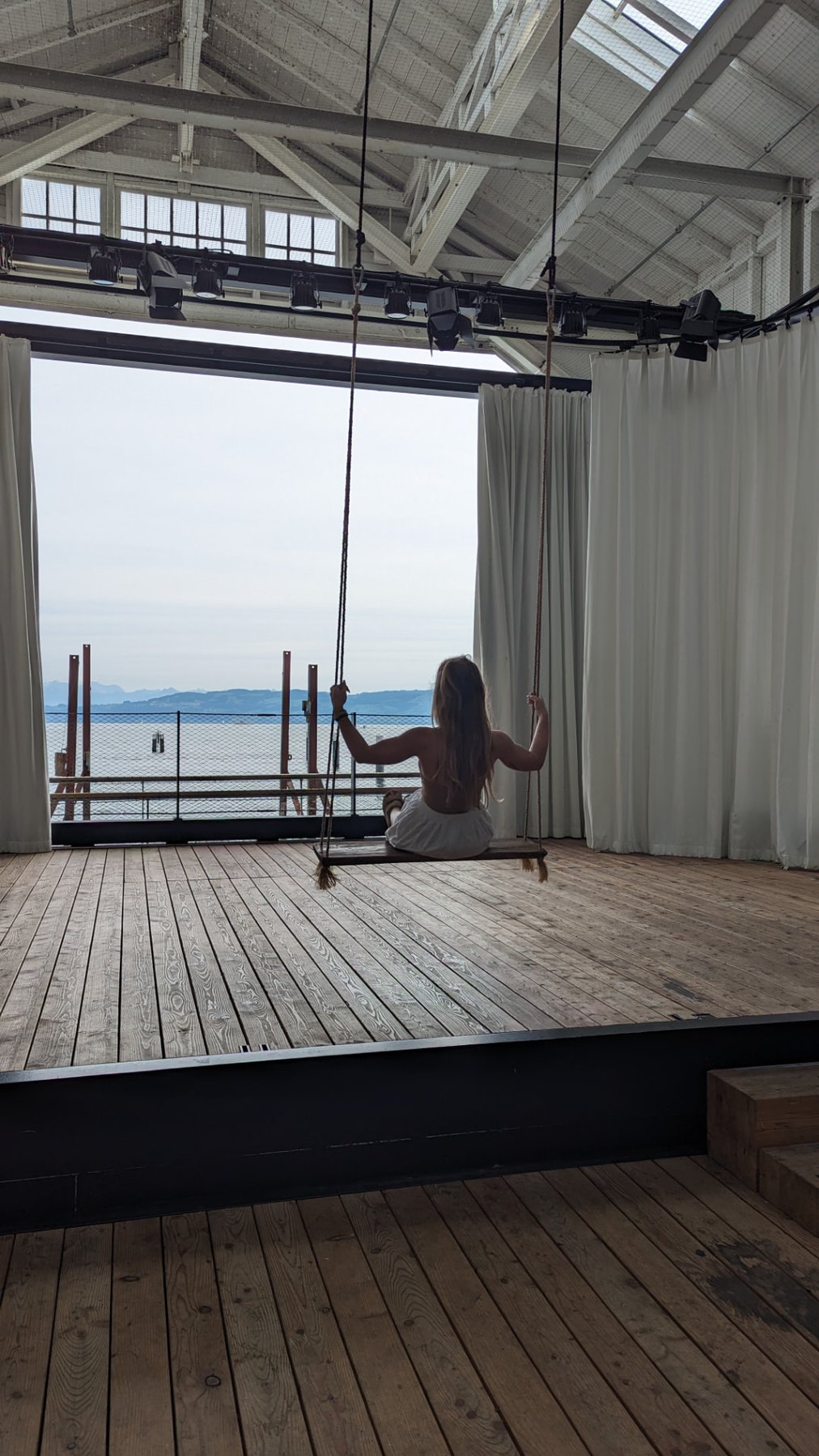 Frau auf einer Holzschaukel mit weitem Blick über den See
